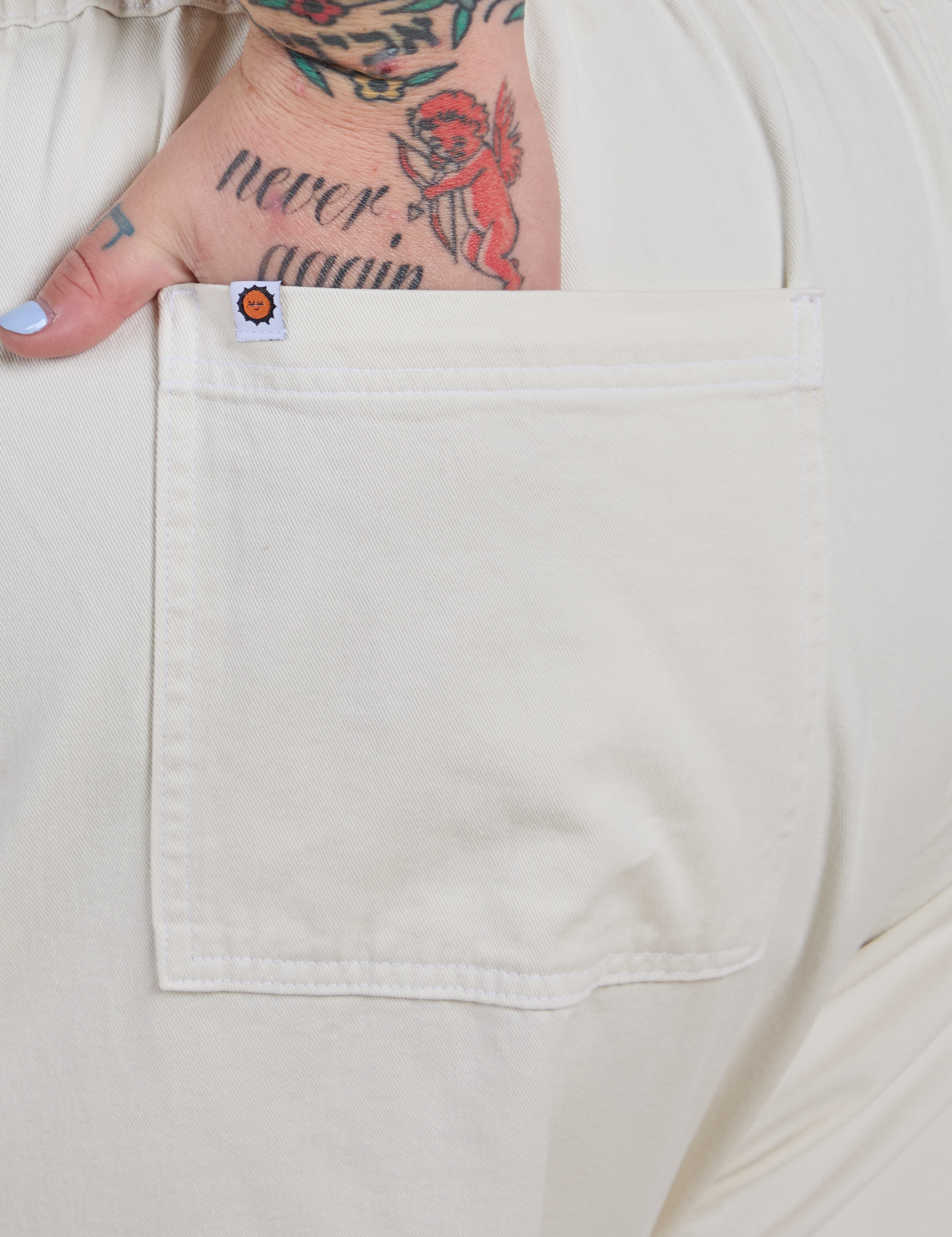 Close up of Sam's hand in the back pocket of Short Sleeve Jumpsuit in Vintage Tee White