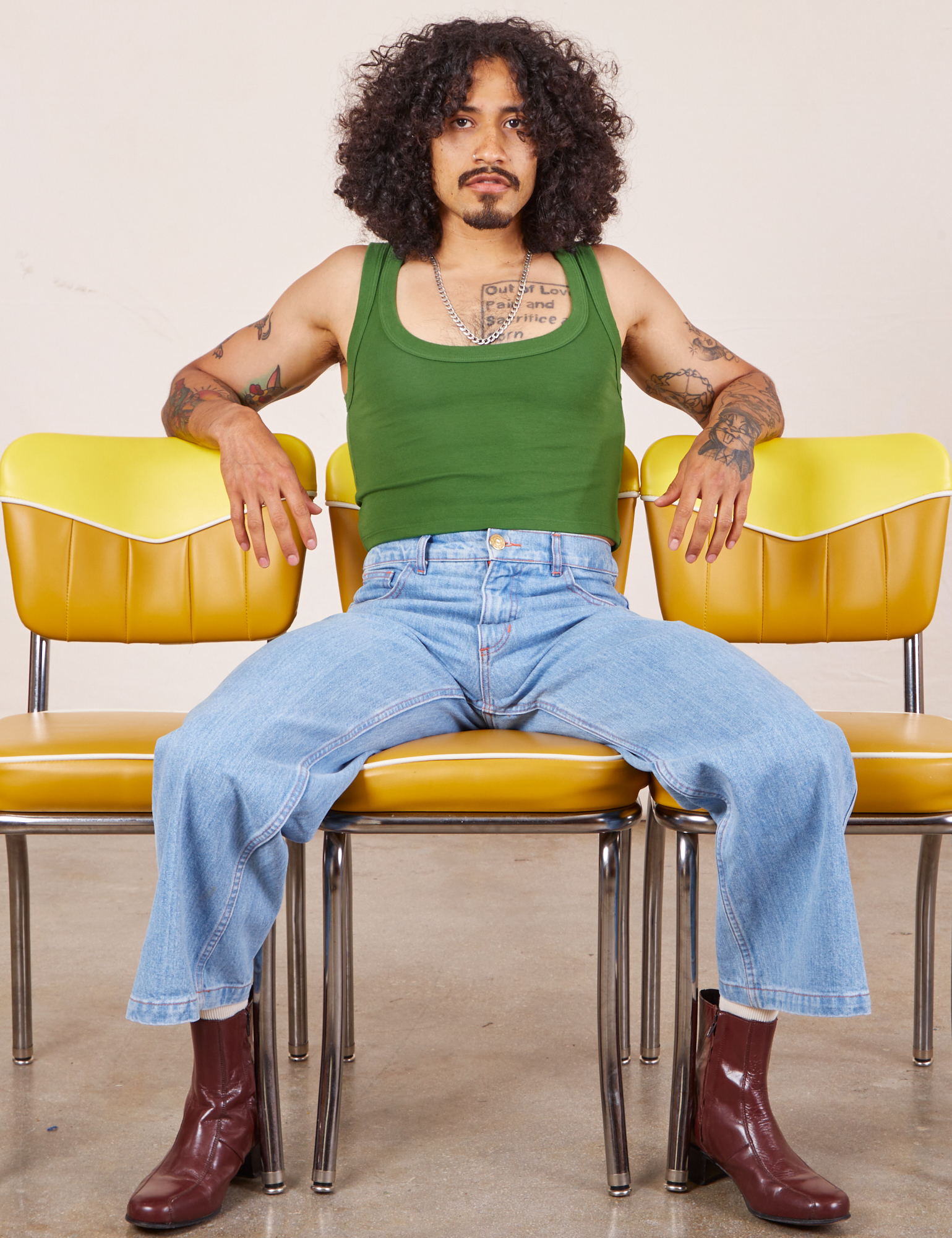 Jesse is wearing Cropped Tank Top in Lawn Green and light wash Sailor Jeans. They are sitting on a yellow chair.