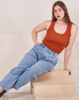 Allison is sitting on a wooden crate wearing Denim Trouser Jeans in Light Wash and a burnt orange Tank Top