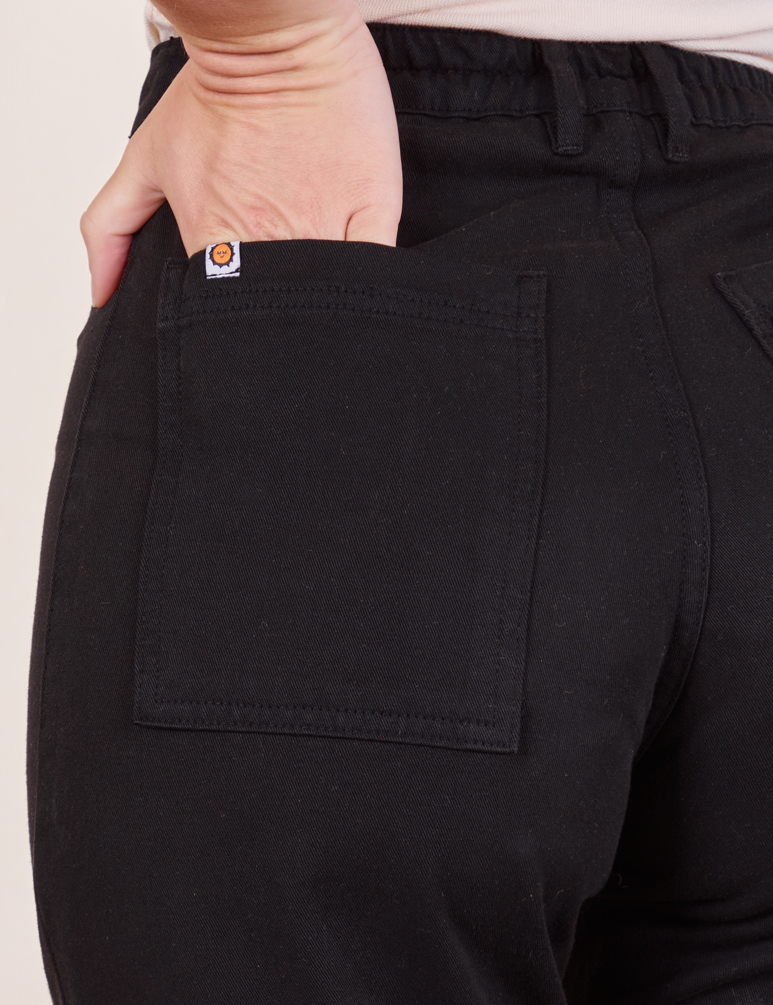 Back pocket close up of Western Pants in Basic Black. Alex has her hand in the pocket