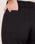 Back pocket close up of Western Pants in Basic Black. Alex has her hand in the pocket