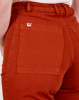 Back pocket close up of Western Pants in Paprika worn by Alex. Sun baby logo tag in white and orange on top edge of pocket.