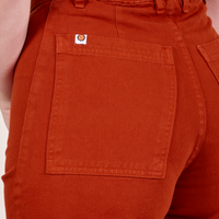 Back pocket close up of Western Pants in Paprika worn by Alex. Sun baby logo tag in white and orange on top edge of pocket.