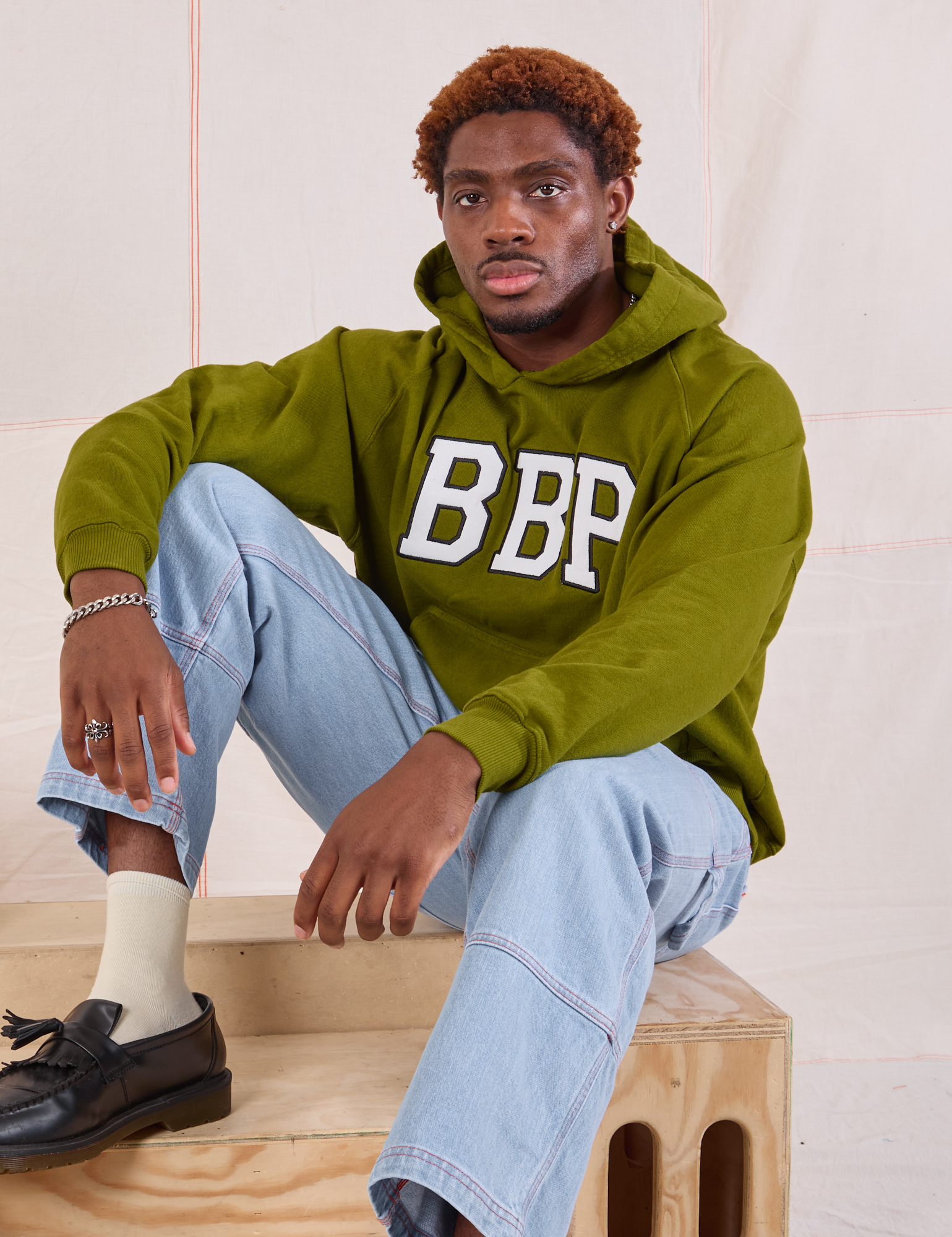 Issac is wearing Collegiate Hoodie in Summer Olive and light wash Carpenter Jeans