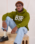 Issac is wearing Collegiate Hoodie in Summer Olive and light wash Carpenter Jeans