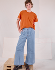 Quinn is wearing Burly Tee in Construction Orange tucked into light wash Denim Wide Leg Trousers