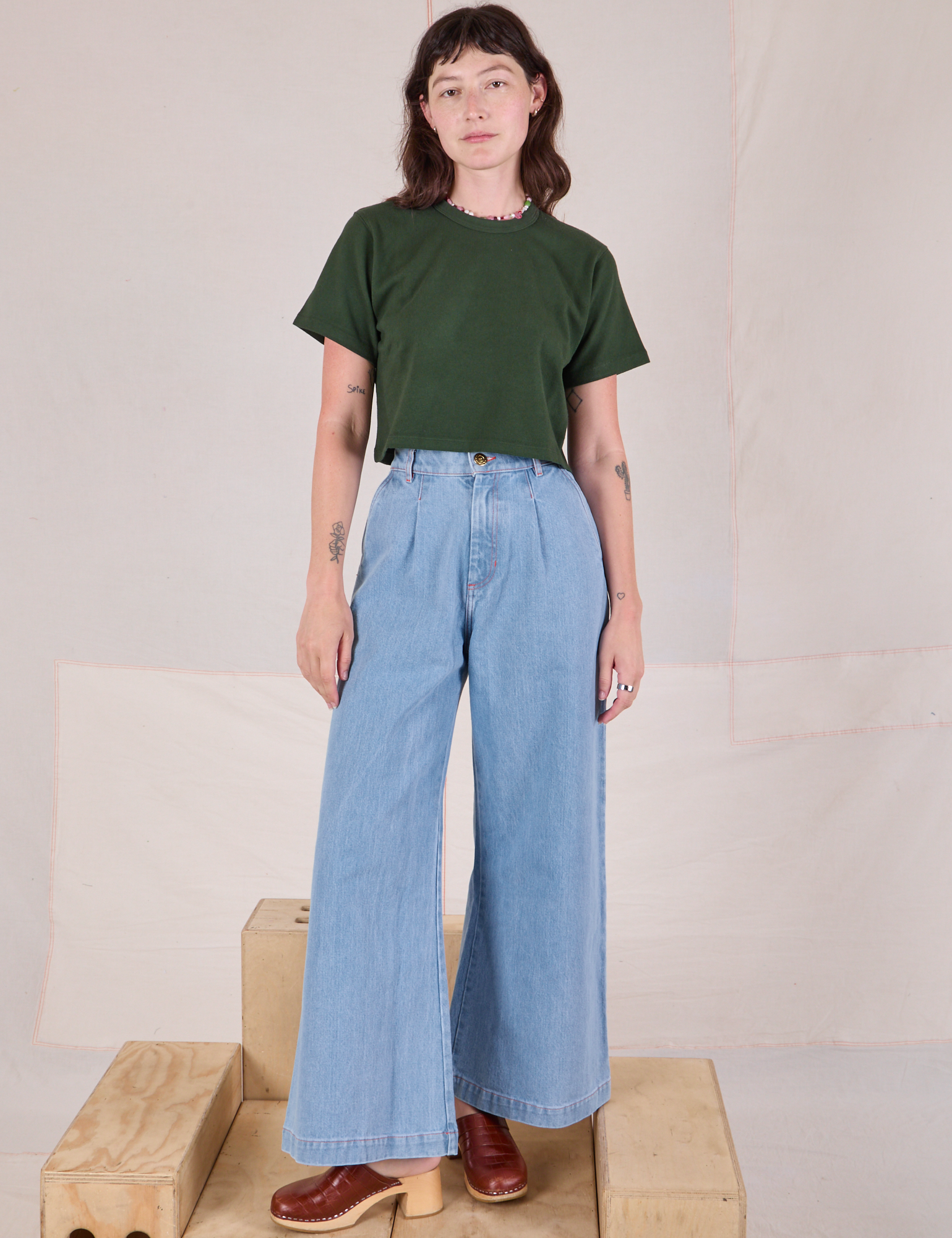 Alex is wearing Cropped Burly Tee in Swamp Green wide leg denim trousers in light wash