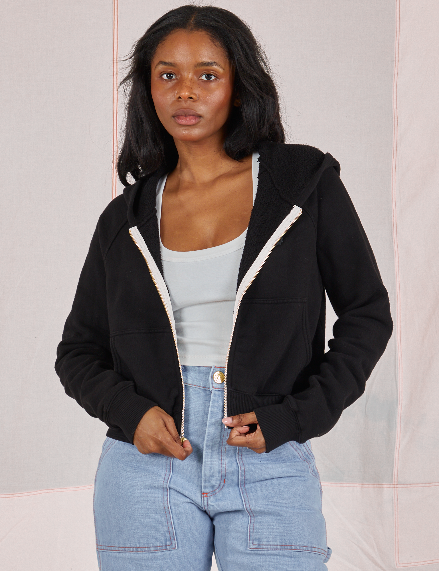 Kandia is 5&#39;3&quot; and wearing P Cropped Zip Hoodie in Basic Black with a vintage off-white Cropped Tank underneath and light wash Carpenter Jeans