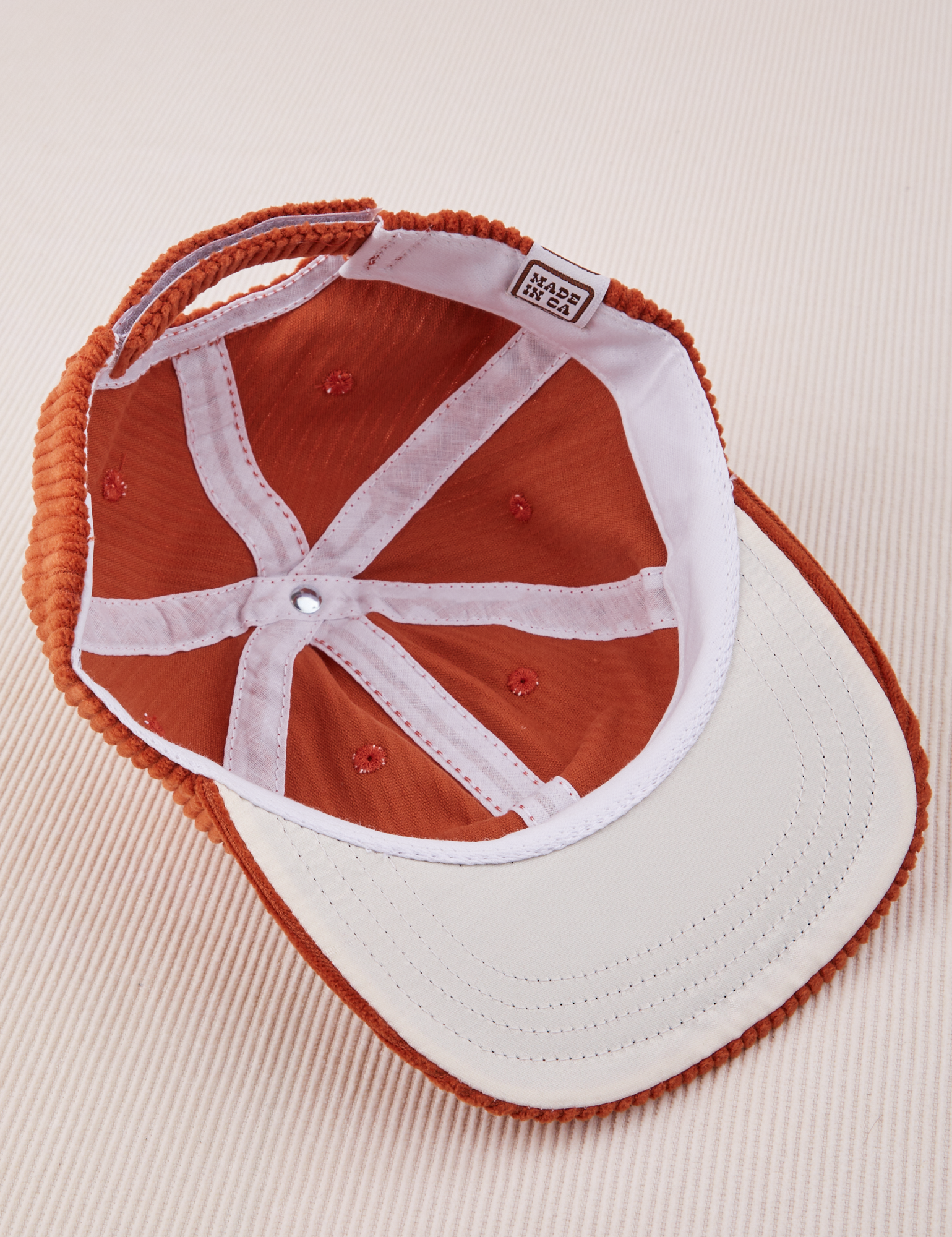 Dugout Corduroy Hat in Burnt Terracotta flipped over. White satin under-bill.