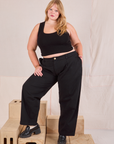 Juliet is 5'7" and wearing 0XL Mid-Rise Pleated Trousers in Basic Black paired with black Cropped Tank