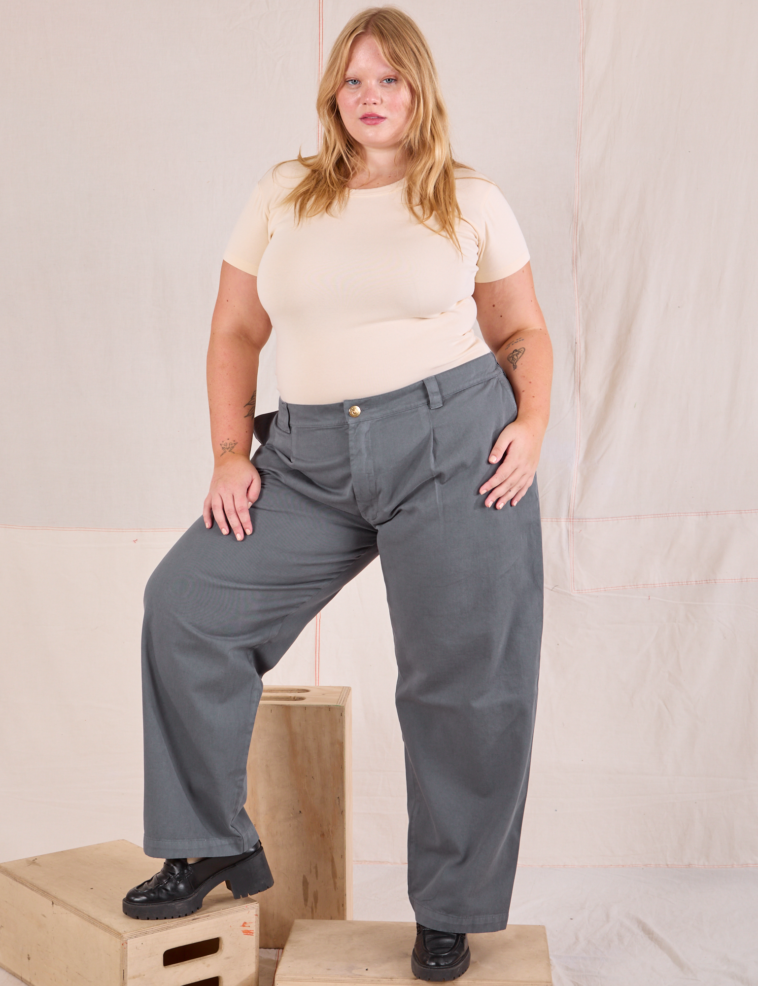 Juliet is 5&#39;7&quot; and wearing 0XL Mid-Rise Pleated Trousers in Slate Grey paired with a Baby Tee in vintage tee off-white