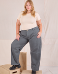 Juliet is 5'7" and wearing 0XL Mid-Rise Pleated Trousers in Slate Grey paired with a Baby Tee in vintage tee off-white