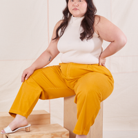 Ashley is sitting on a wooden crate wearing Organic Trousers in Mustard Yellow and vintage off-white Sleeveless Essential Turtleneck