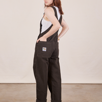 Angled back view of Original Overalls in Mono Espresso. Hana has both hands in the back pockets.