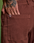 Close up of Jesse's hand in the back pocket of Paintstamped Work Pants in Mushroom