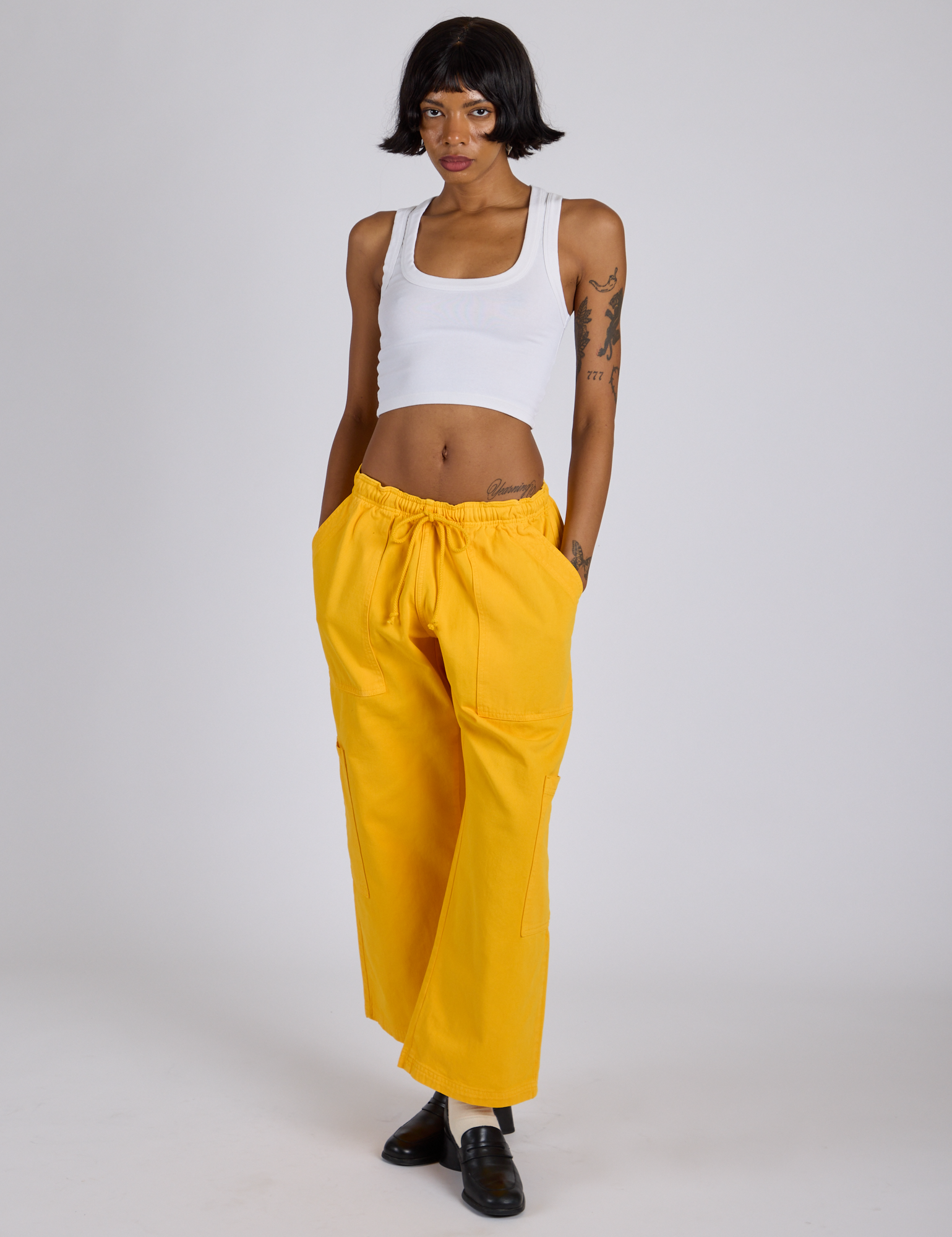 Kira is 5’10” and wearing XS Drop Pocket Cargo Pants in Sunshine Yellow paired with a Cropped Tank in Vintage Tee White