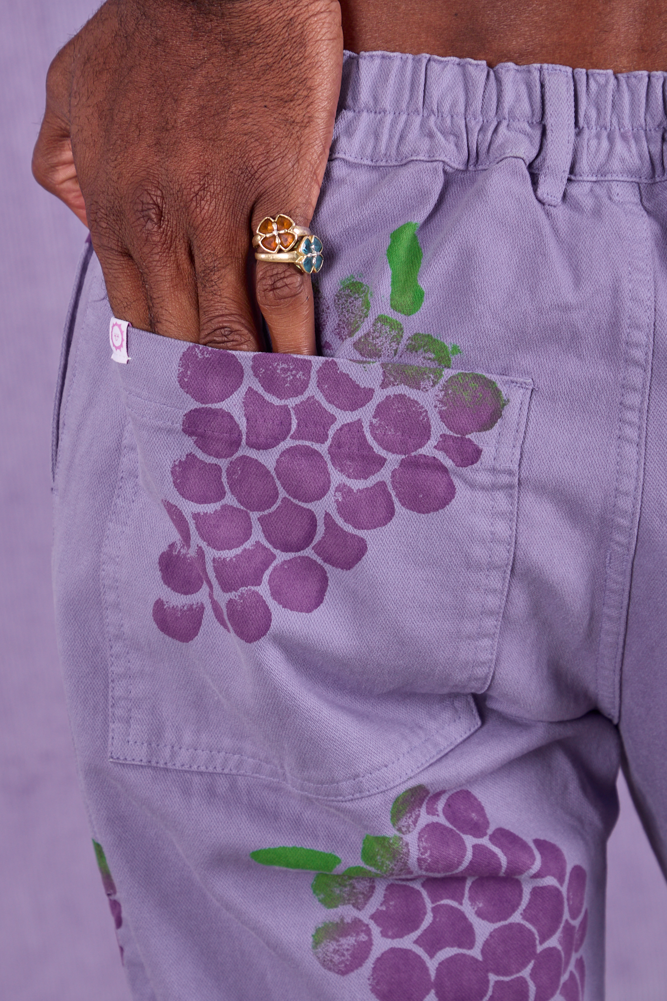 Close up of Jerrod&#39;s hand tucked into the back pocket of Paintstamped Work Pants in Grape
