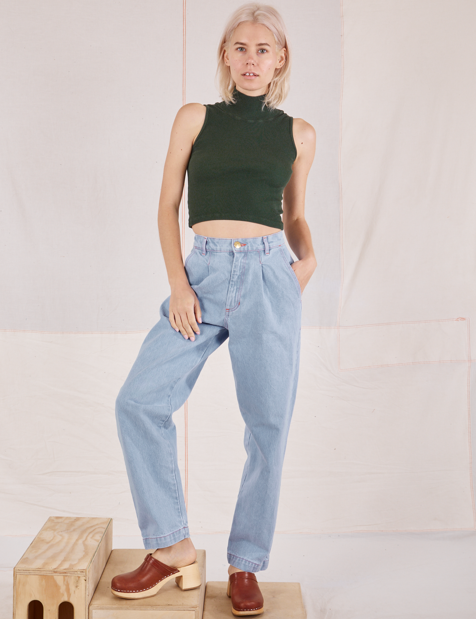 Madeline is wearing Sleeveless Essential Turtleneck in Swamp Green and light wash Denim Trouser Jeans