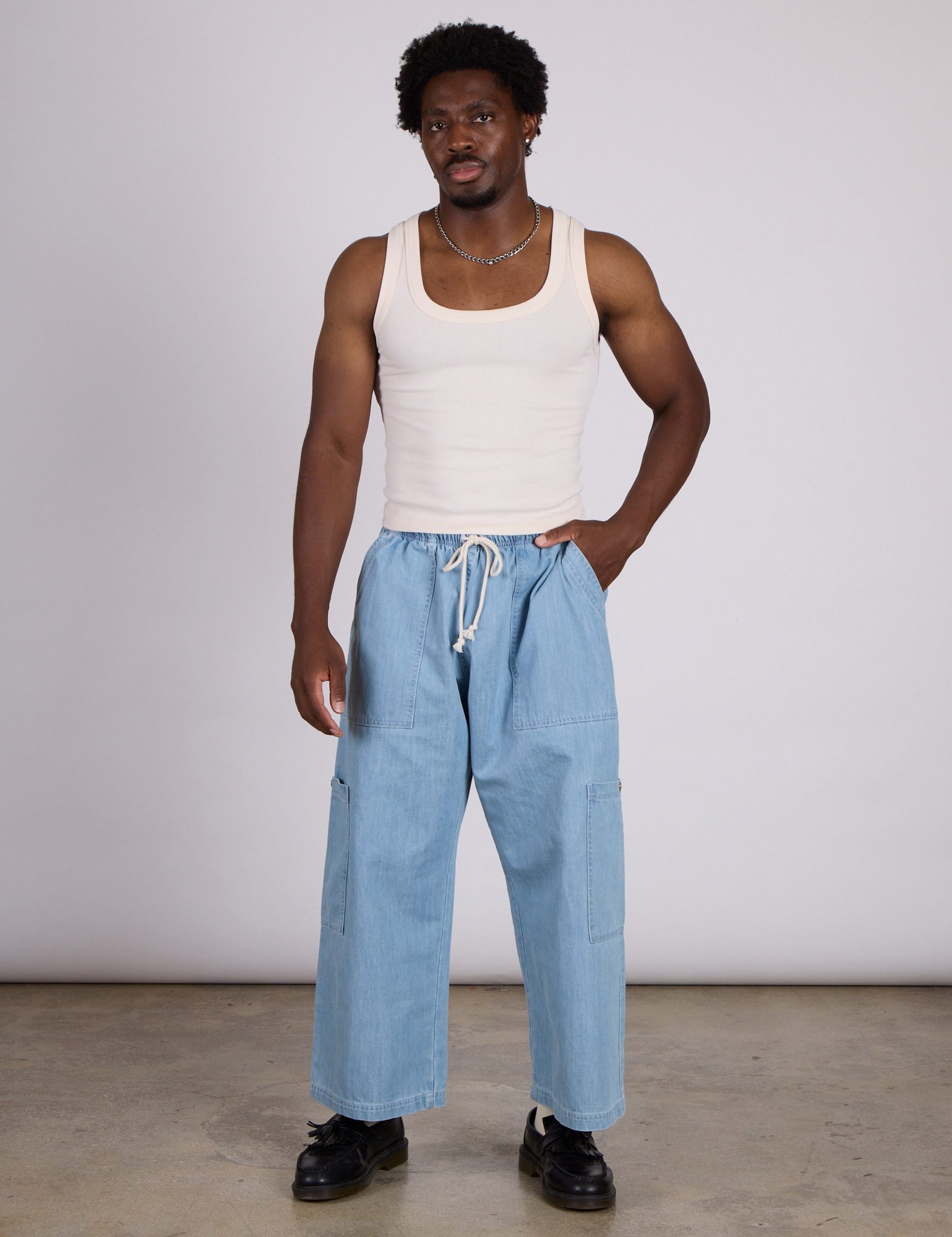 Isaac is wearing The Tank Top in Vintage Tee Off-White and light wash denim drop pocket pants
