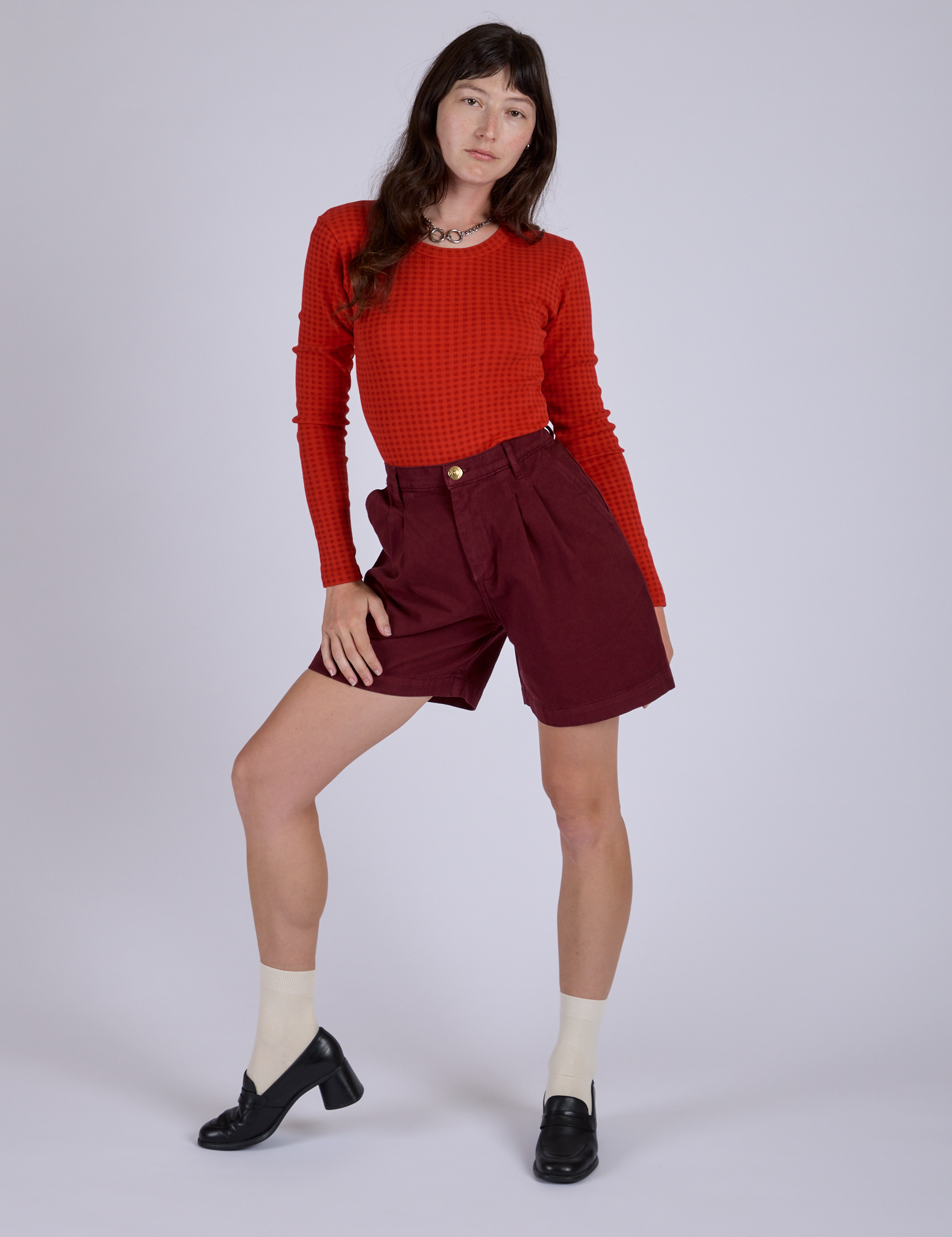 Alex is 5’8” and wearing XXS Pleated Trouser Shorts in Red Wine paired with mustang red Long Sleeve Gingham Baby Tee