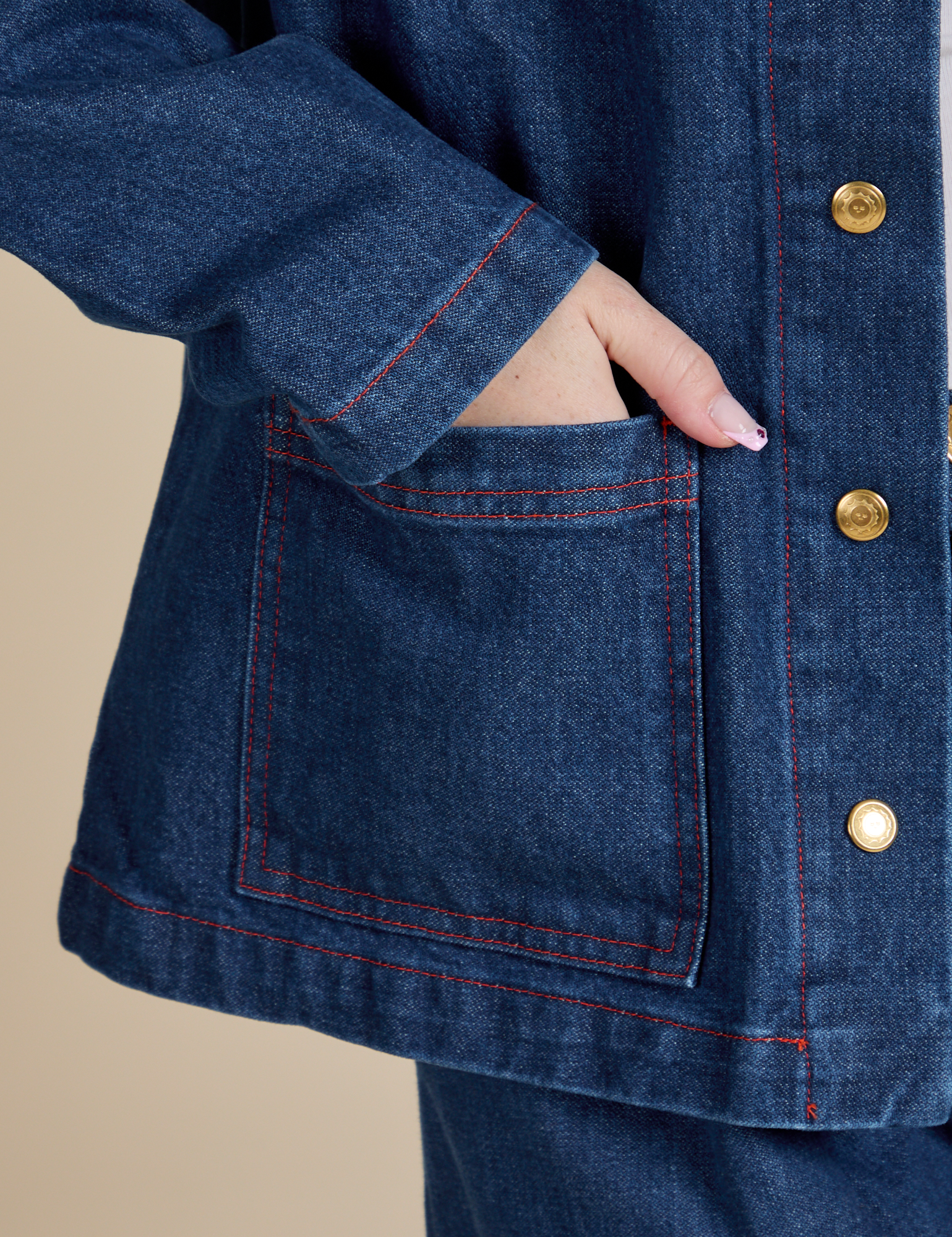 Close up of Hana's hand in the front bottom pocket of Indigo Denim Work Jacket in Dark Wash