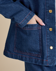 Close up of Hana's hand in the front bottom pocket of Indigo Denim Work Jacket in Dark Wash