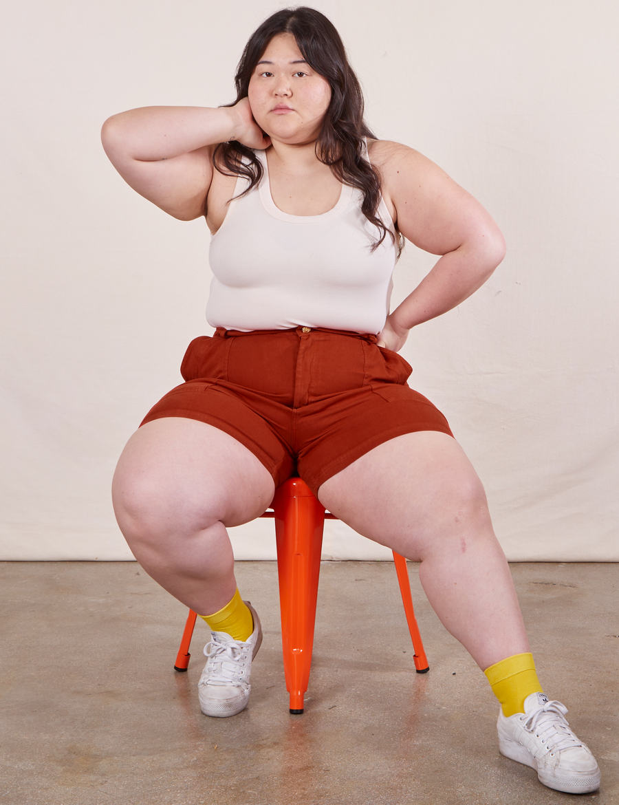 Ashley is sitting in an orange metal stool. She is wearing Classic Work Shorts in Paprika paired with vintage off-white Tank Top.