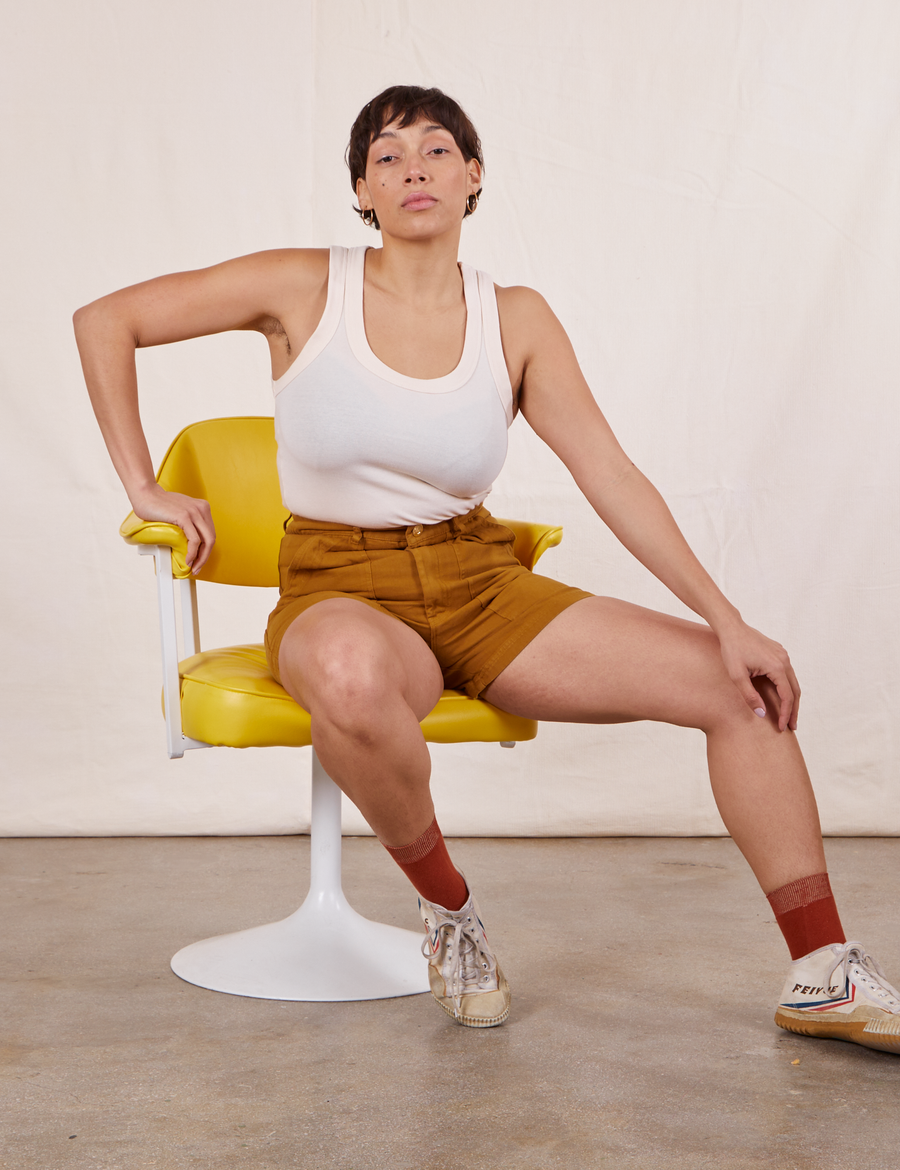 Tiara is sitting in a yellow chair wearing Classic Work Shorts in Spicy Mustard and vintage off-white Tank Top