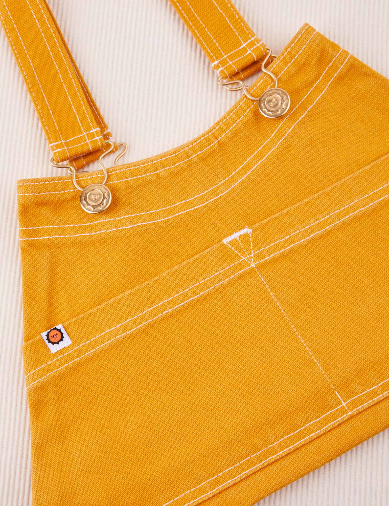 Overall Handbag in Mustard Yellow. Contrast white stitching. Brass sun baby buttons and hardware.