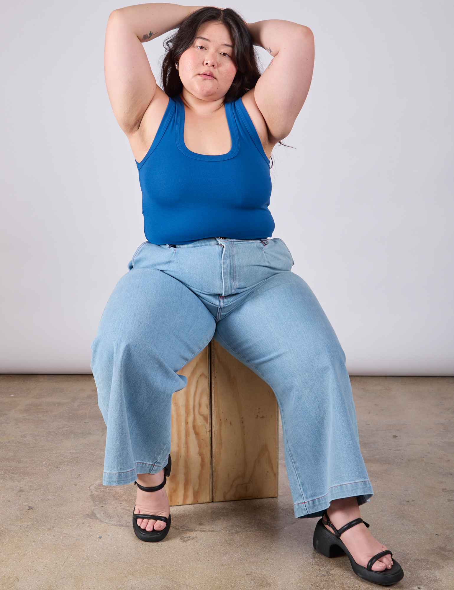 Ashley is sitting on a wooden block and wearing Cropped Tank Top in Royal Blue paired with light wash Indigo Wide Leg Trousers