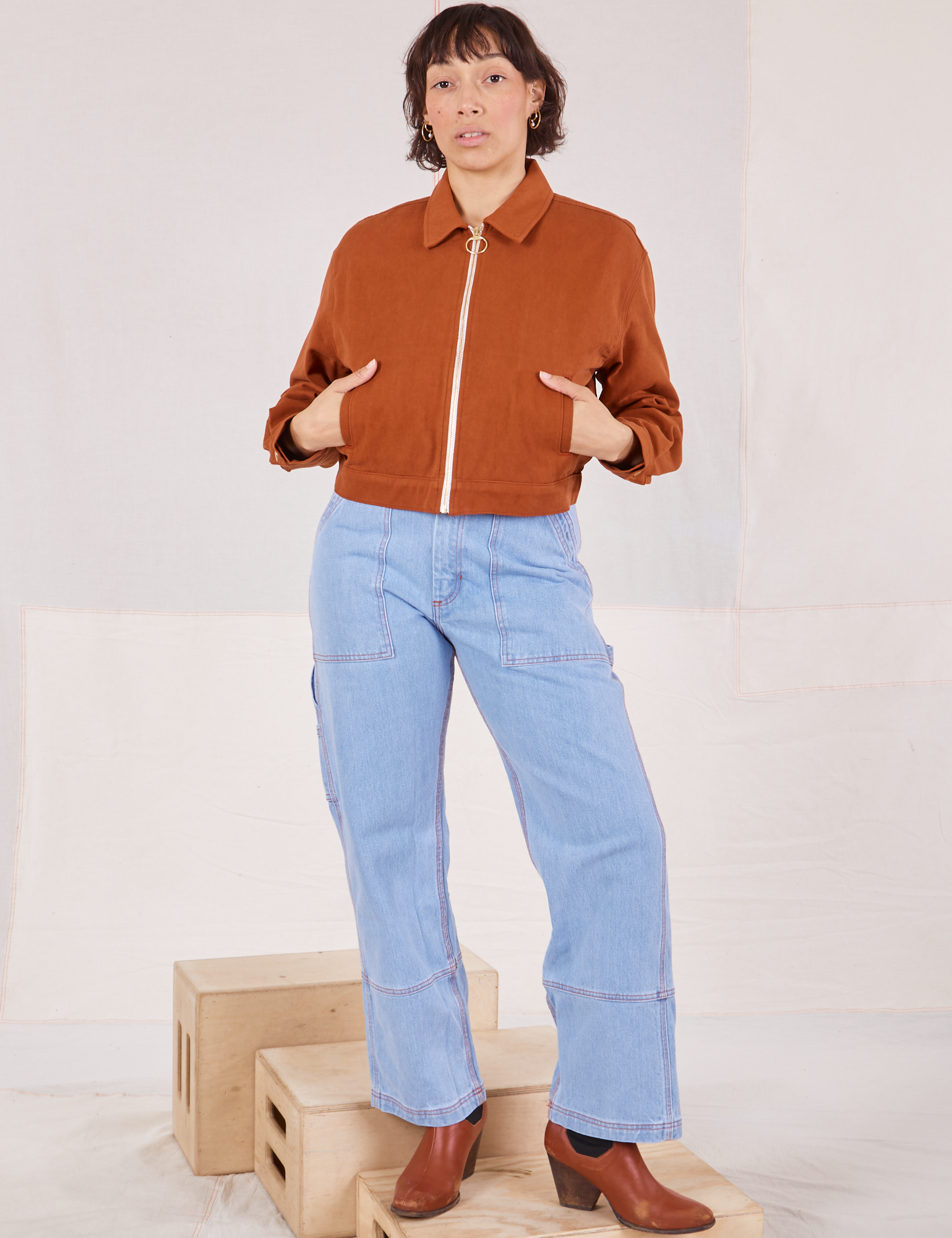 Tiara is wearing a zipped up Ricky Jacket in Burnt Terracotta and light wash Carpenter Jeans