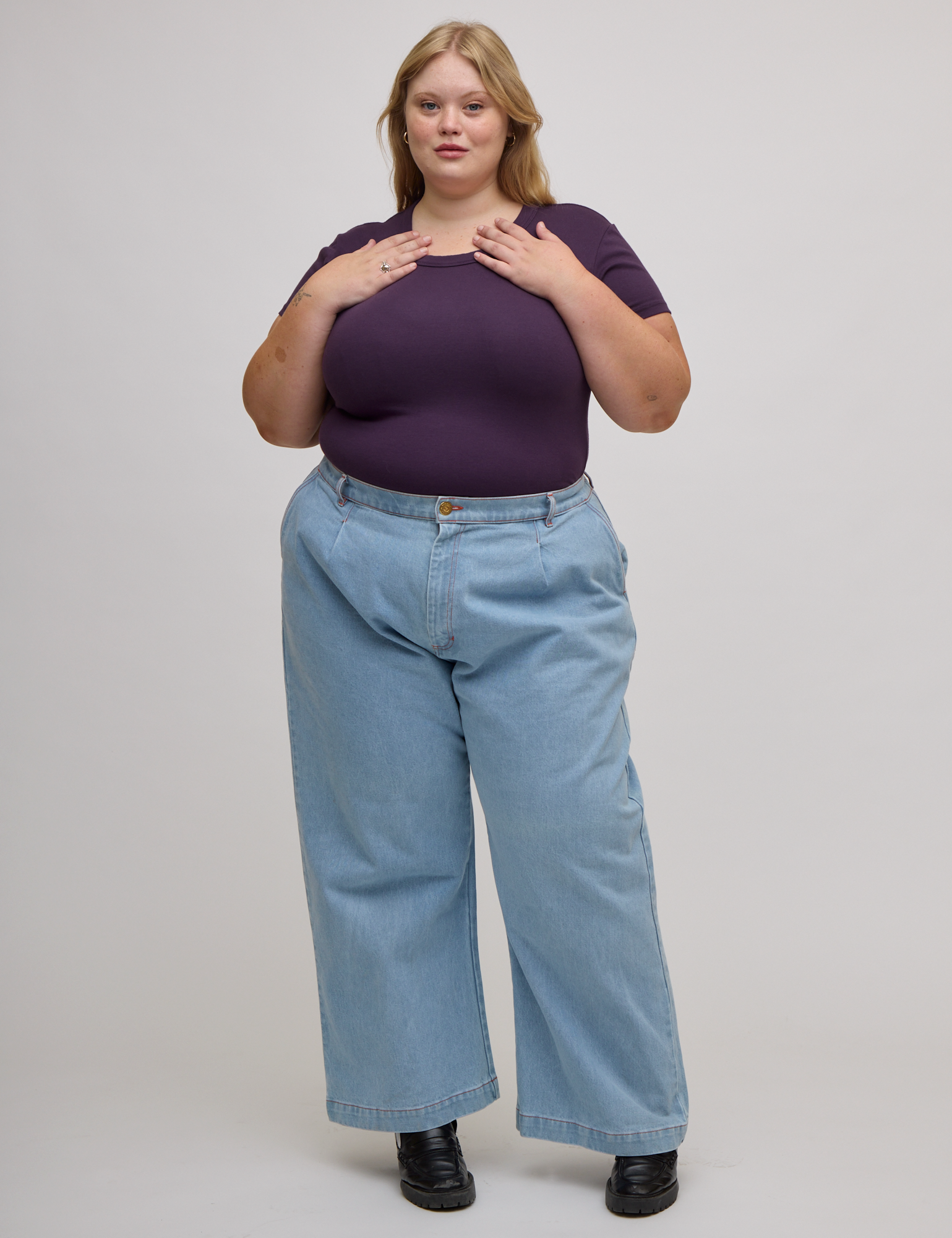 Juliet is wearing Baby Tee in Nebula Purple tucked into light wash wide leg trousers
