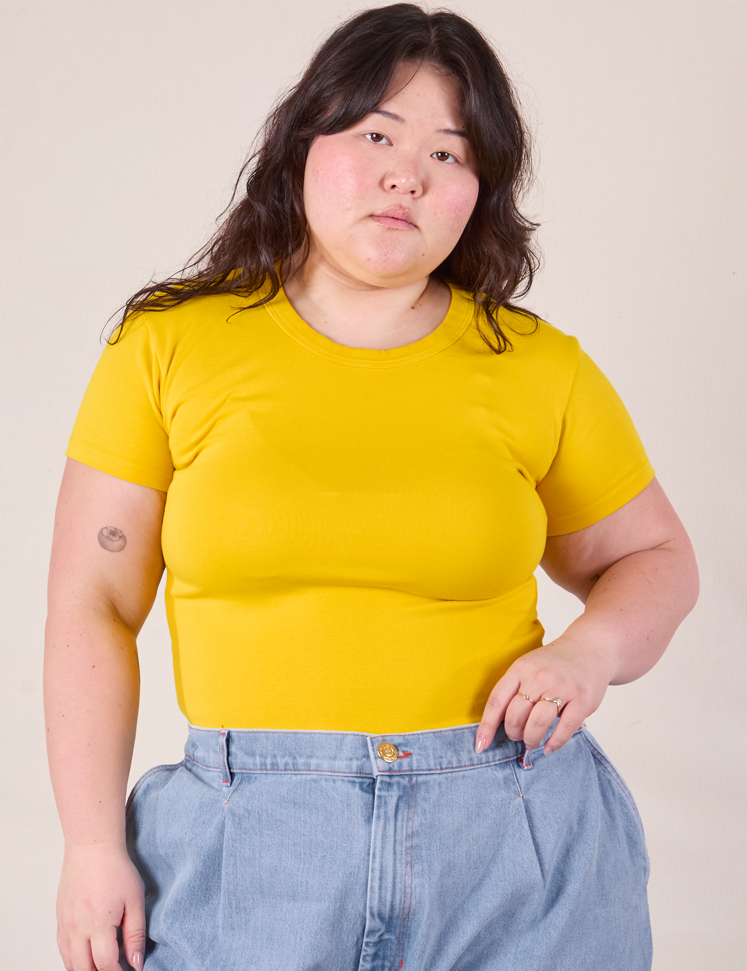 Ashley is wearing Baby Tee in Golden Yellow tucked into denim Trousers