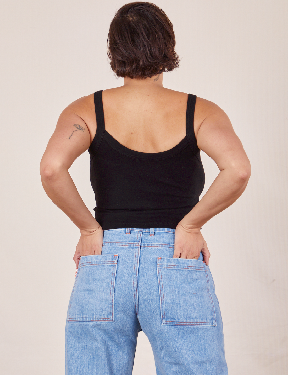 Back view of Cropped Cami in Basic Black and light wash Sailor Jeans worn by Tiara. She has both her hands in the back pant pockets.
