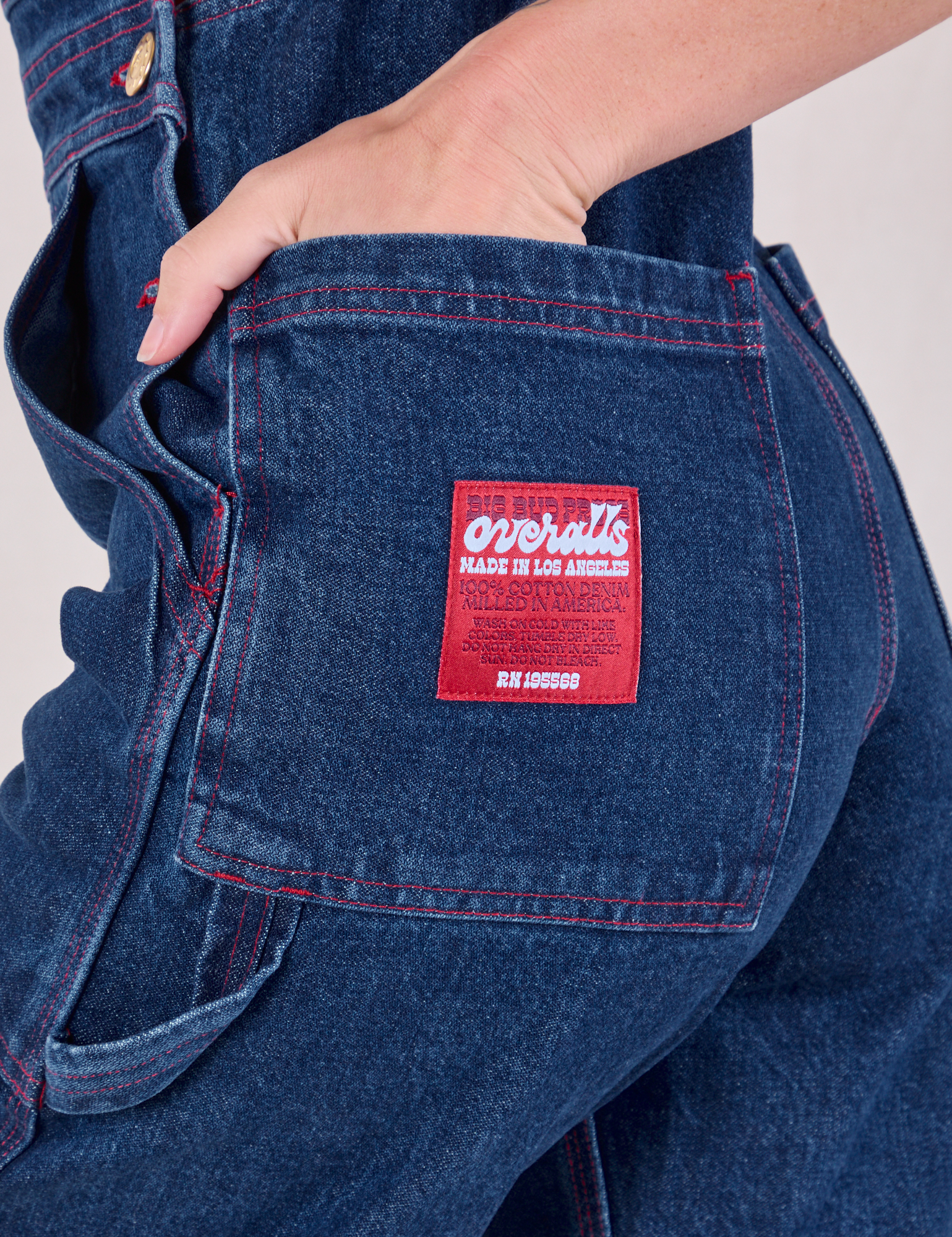 Close up of Alex&#39;s hand in the back pocket of Carpenter Overalls in Dark Wash