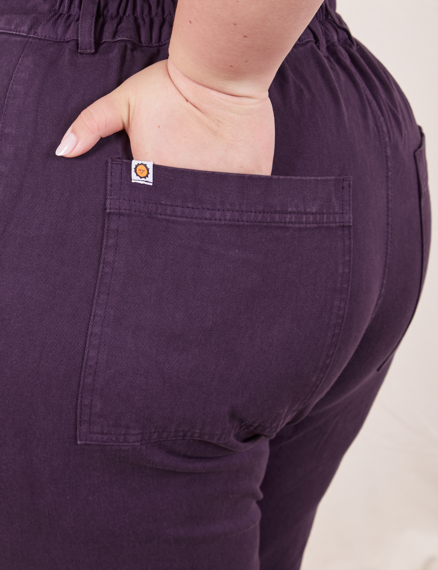 Back pocket close up of Short Sleeve Jumpsuit in Nebula Purple. Ashley has her hand in the pocket.