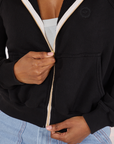 Cropped Zip Hoodie in Basic Black front close up. Kandia is holding onto the zipper tab
