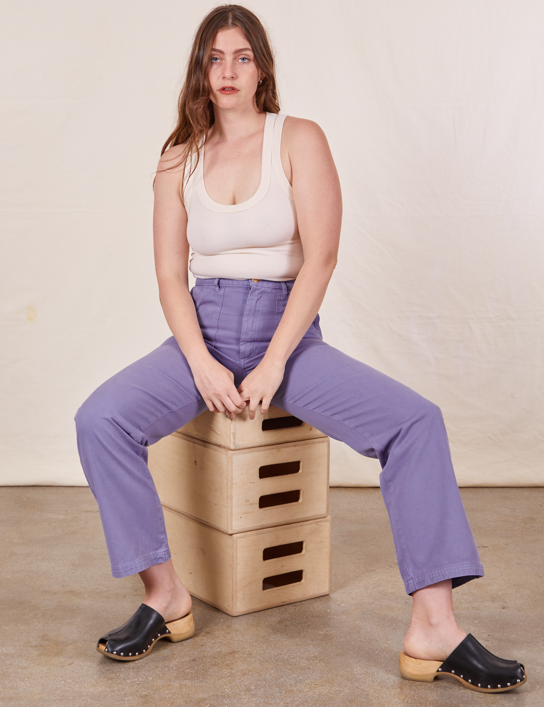Allison is sitting on a stack of wooden crates wearing Work Pants in Faded Grape and a vintage off-white Tank Top
