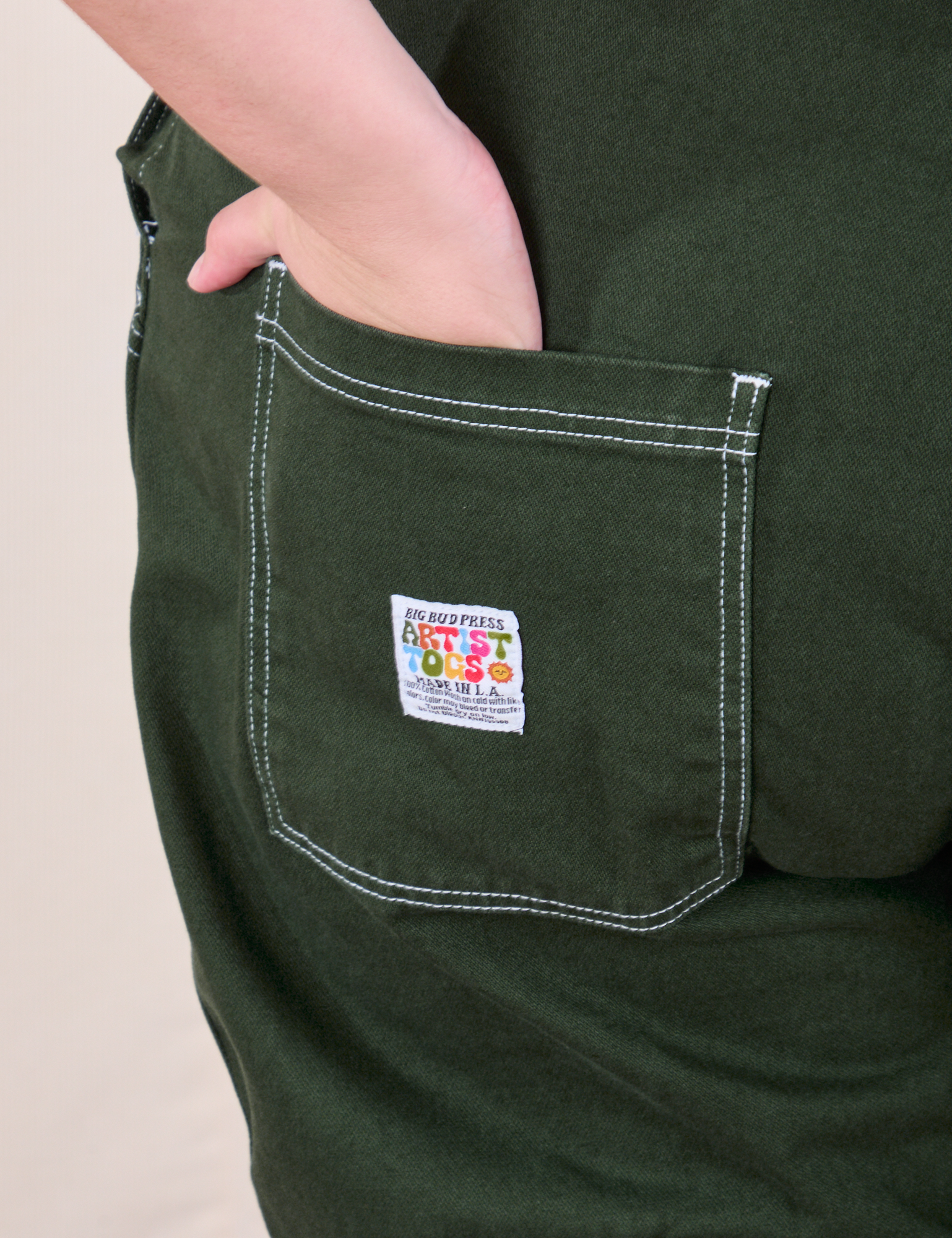 Original Overalls in Swamp Green back pocket close up. Marielena has her hand in the pocket.