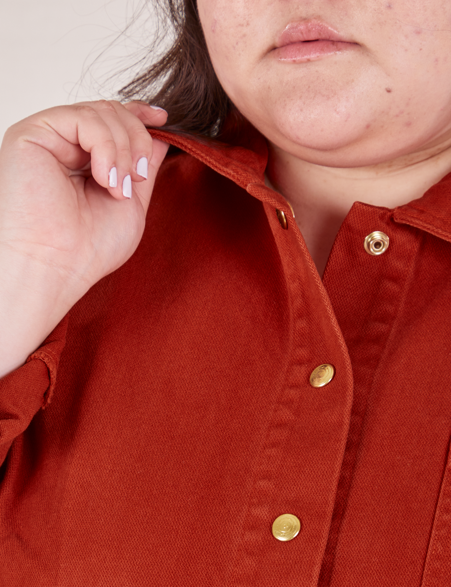 Front close up of Denim Work Jacket in Paprika worn by Ashley. She is holding the edge of the jacket collar. Brass buttons on jacket.