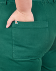 Back pocket close up of Short Sleeve Jumpsuit in Hunter Green. Marielena has her hand in the pocket.