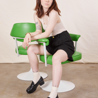 Hana is sitting in a vintage green and white chair wearing Trouser Shorts in Basic Black and a vintage off-white Tank Top