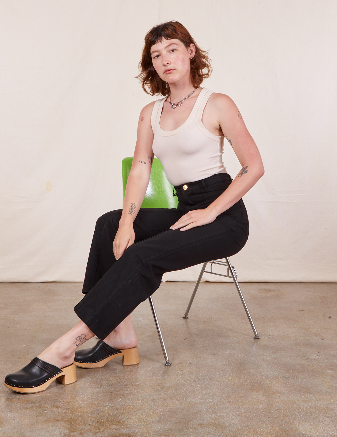 Alex is sitting in a green chair wearing Western Pants in Basic Black and vintage off-white Tank Top