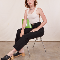 Alex is sitting in a green chair wearing Western Pants in Basic Black and vintage off-white Tank Top