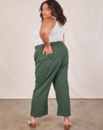 Angled view of Western Pants in Dark Green Emerald and vintage off-white Tank Top worn by Alicia. She also has one hand in the back pocket