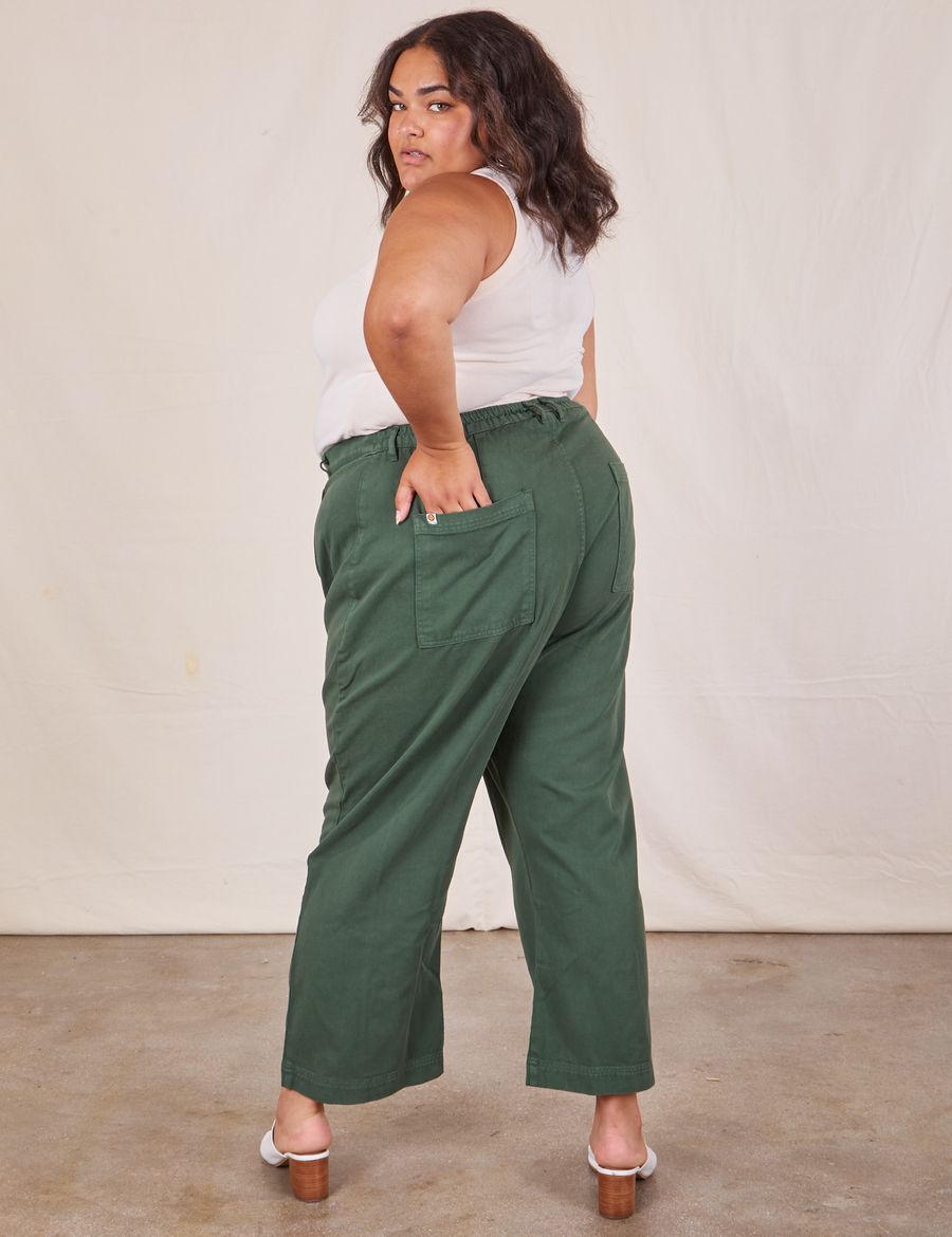 Angled view of Western Pants in Dark Green Emerald and vintage off-white Tank Top worn by Alicia. She also has one hand in the back pocket