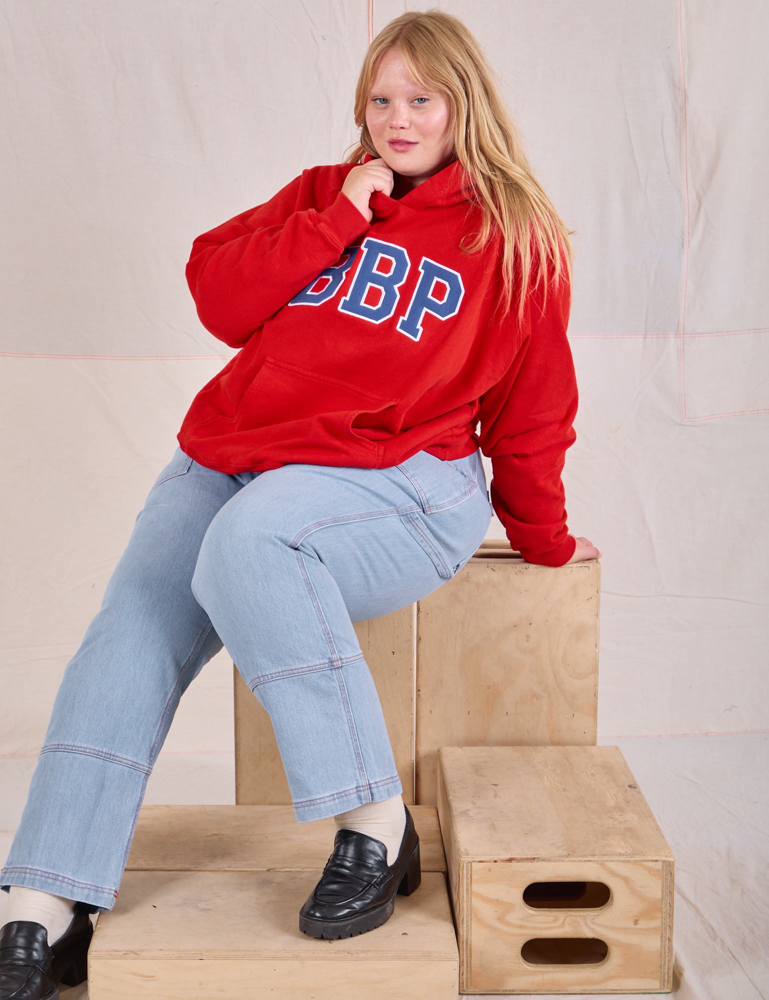 Juliet is wearing Collegiate Hoodie in Mustang Red and light wash Carpenter Jeans