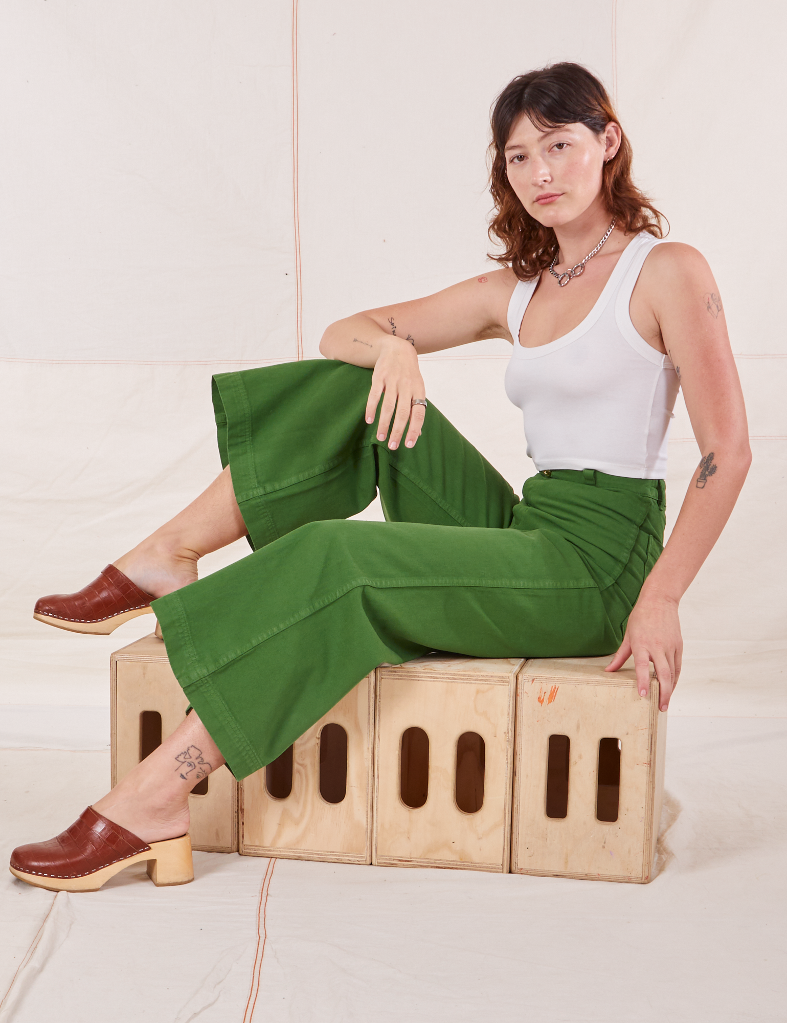 Alex is sitting on a wooden crates. She is wearing  Bell Bottoms in Lawn Green and vintage off-white Cropped Tank Top