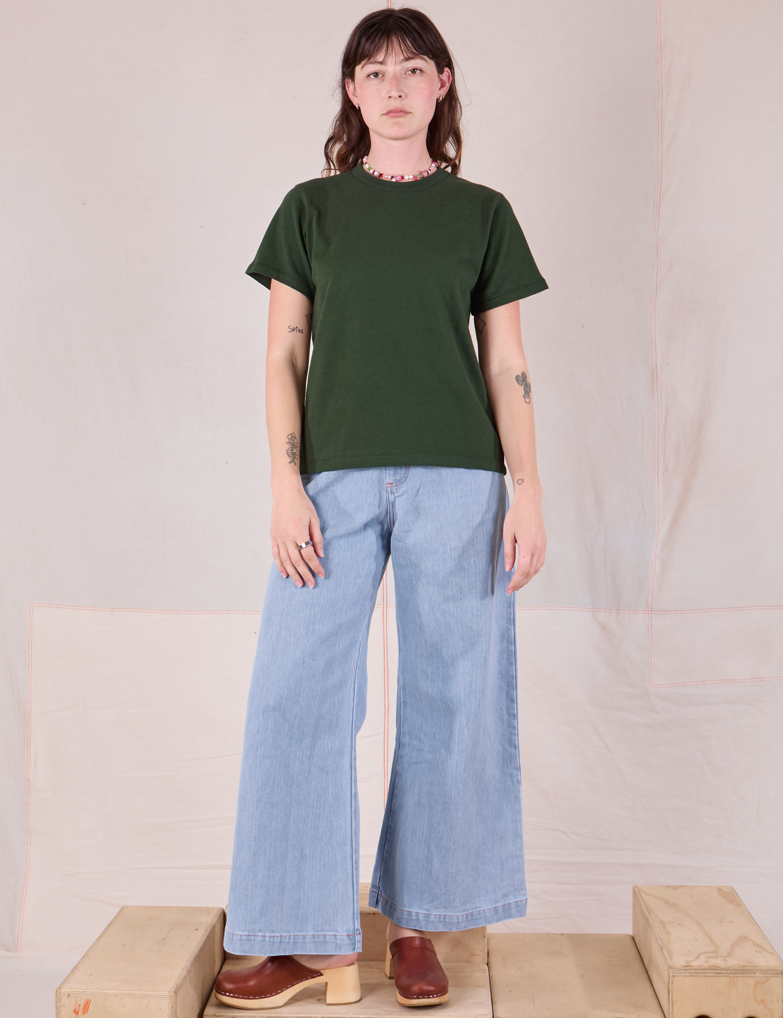 Alex is wearing Burly Tee in Swamp Green paired with light wash Denim Wide Leg Trousers