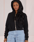 Kandia is wearing Cropped Zip Hoodie in Basic Black with the hood up and light wash Carpenter Jeans